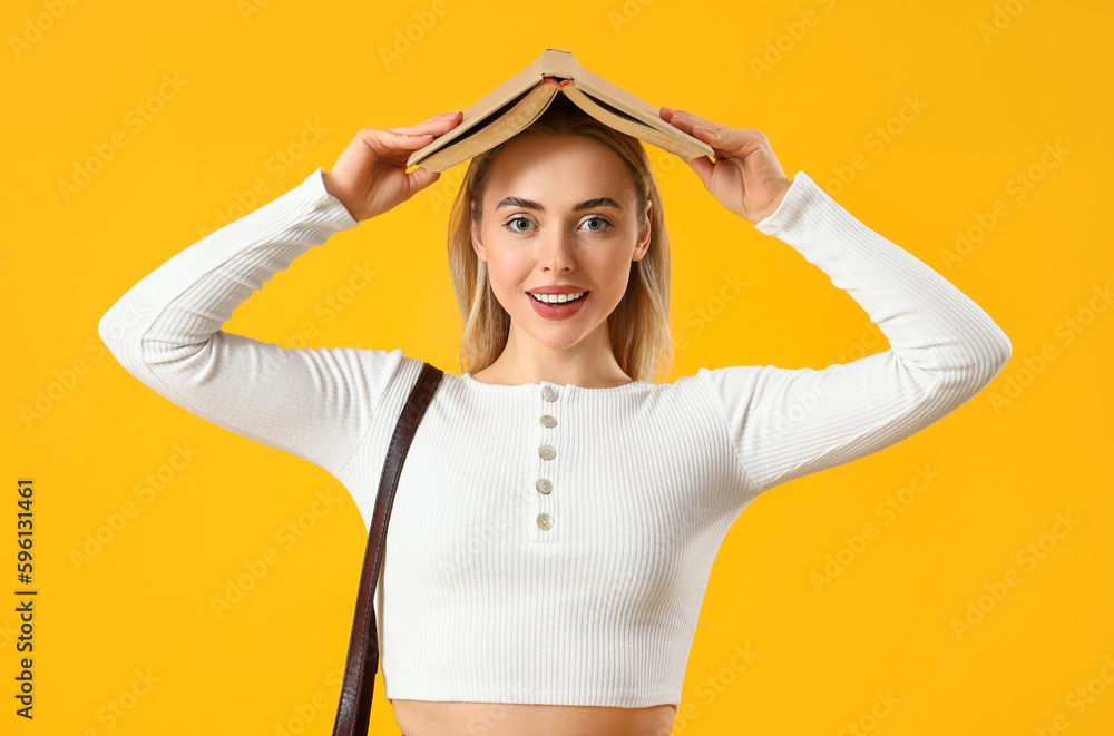 Female student with book on yellow background