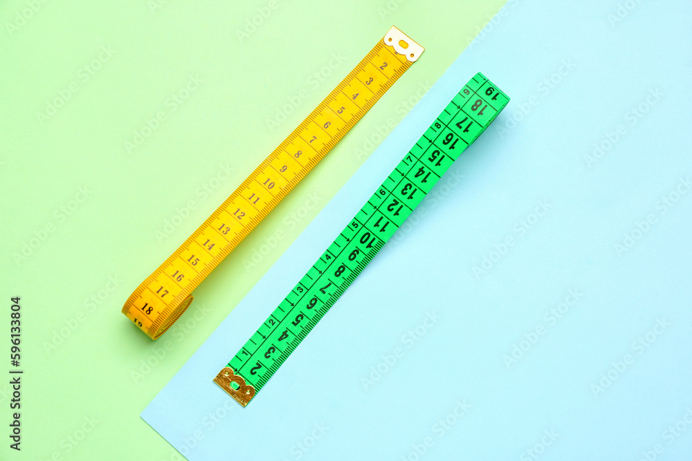 Yellow and green measuring tapes on color background