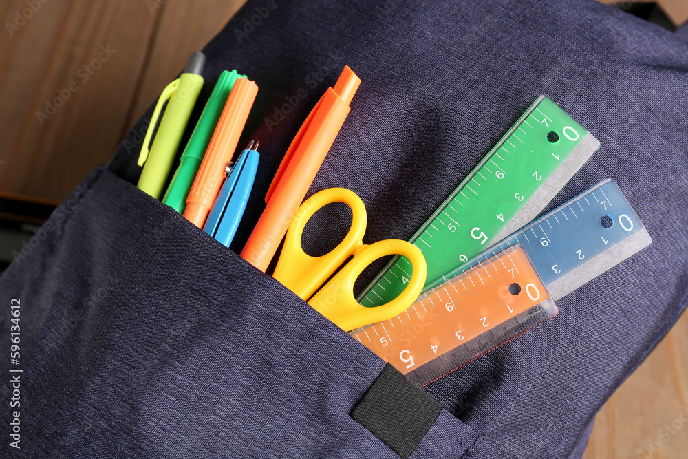 Backpack and stationery supplies on wooden background