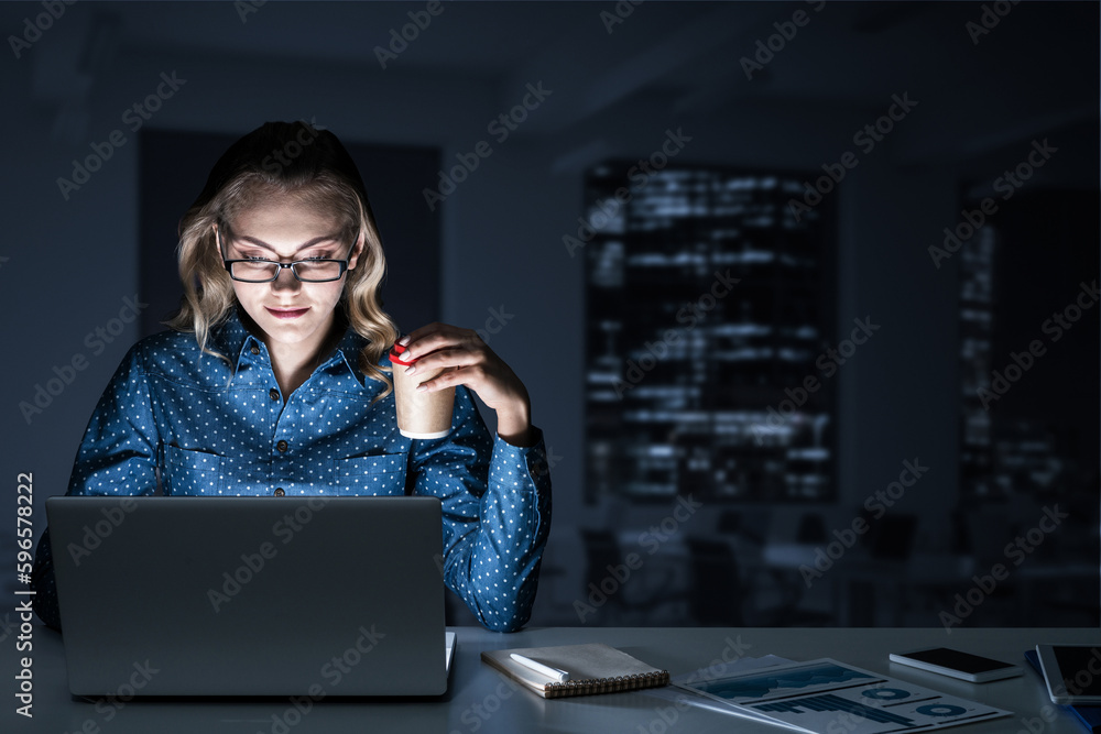 Attractive blonde working on laptop in dark office. Mixed media