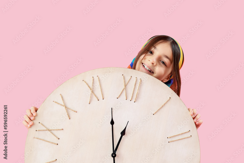 Little girl with big wall clock on pink background