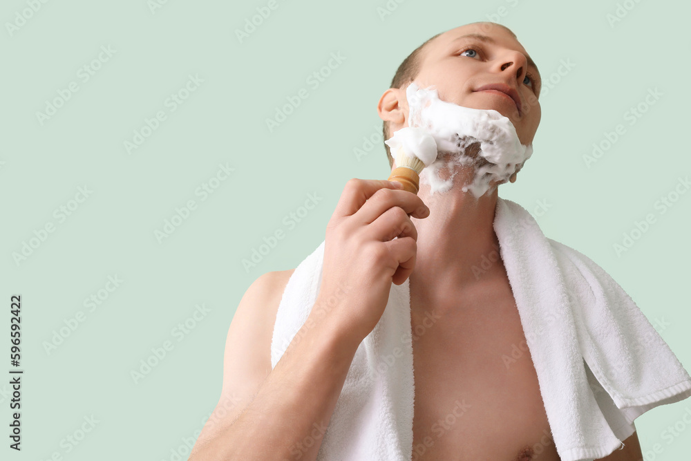 Young man shaving against green background