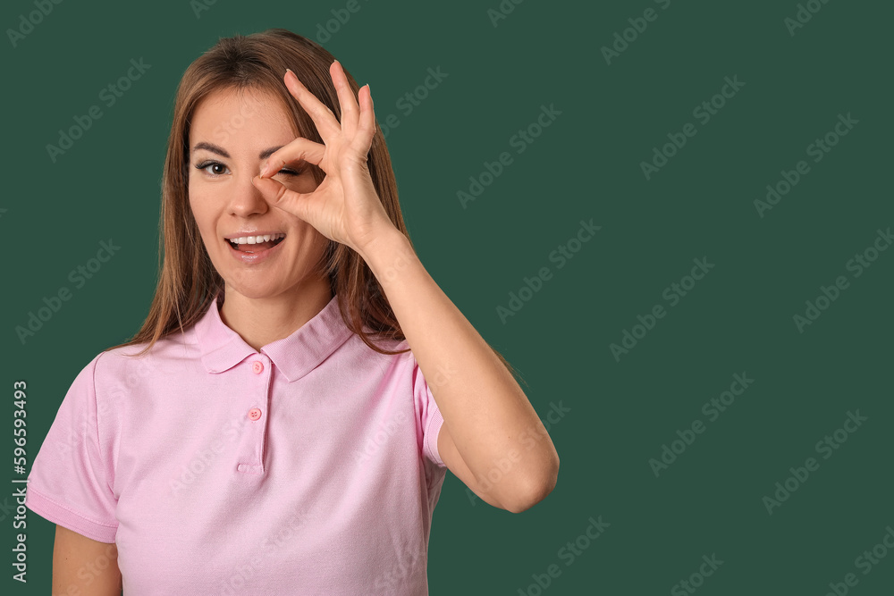 Beautiful woman in pink t-shirt showing OK on green background