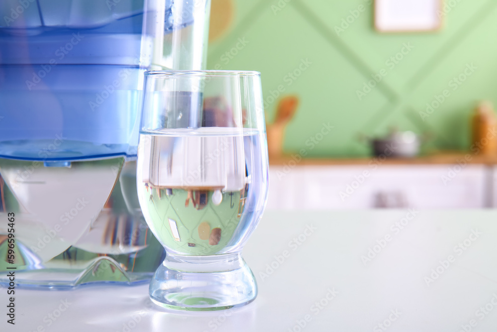 Modern filter jug and glass of water on table in kitchen