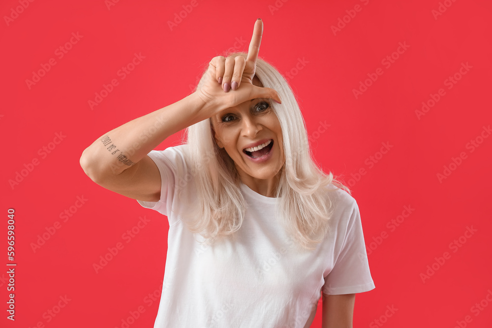 Mature woman showing loser gesture on red background