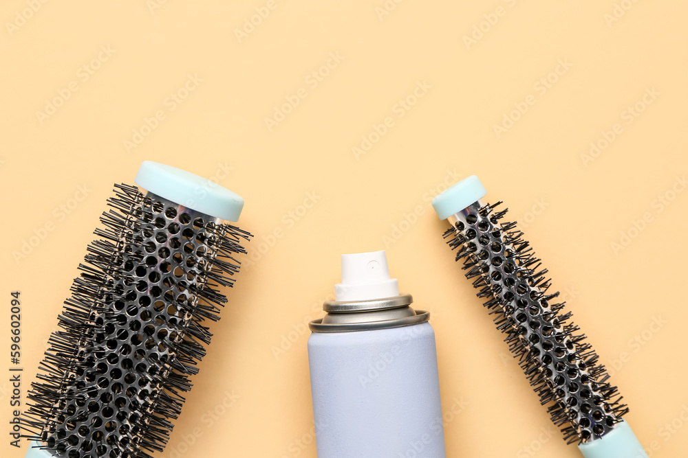 Hairdressers brushes with spray on beige background, closeup