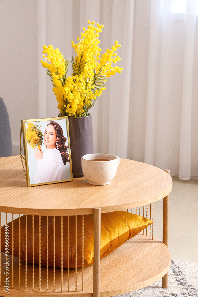 Coffee table with flower vase, cup and photo of woman in interior of living room