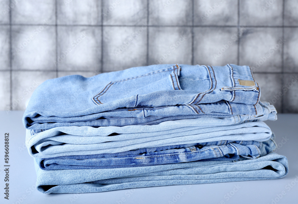 Stack of jeans on table near grey tile wall