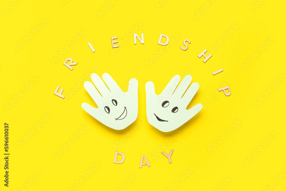 Palms with happy faces and text FRIENDSHIP DAY on yellow background