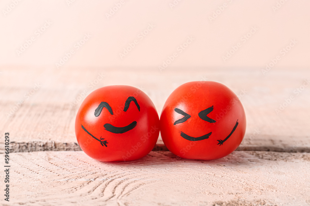 Tomatoes with happy faces on white wooden table. Friendship Day celebration