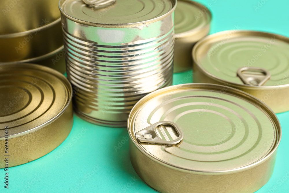 Tin cans with fish on turquoise background, closeup