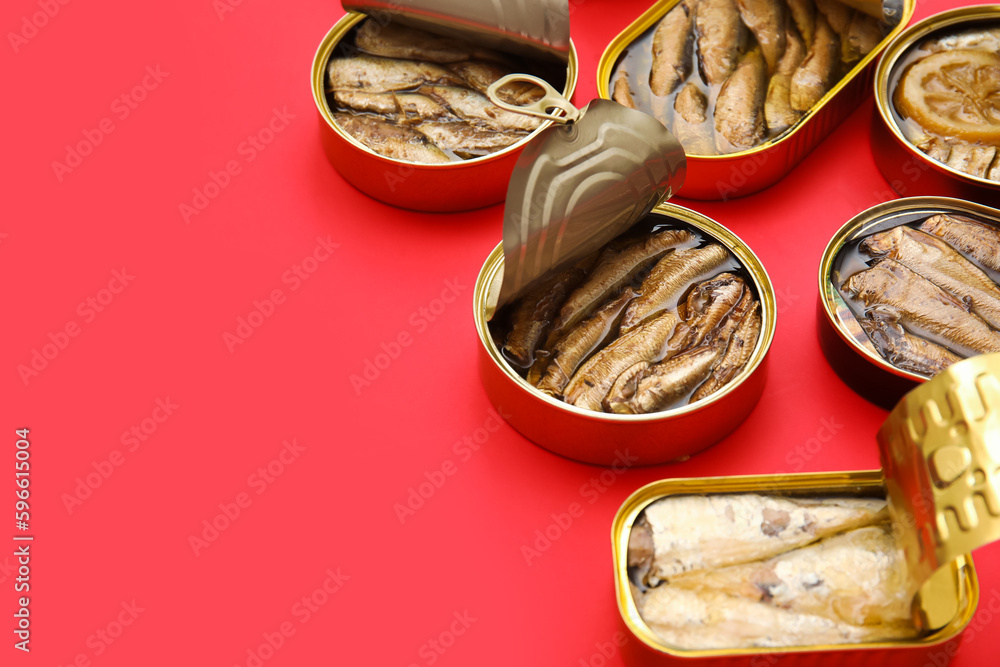 Opened tin cans with different fish on red background