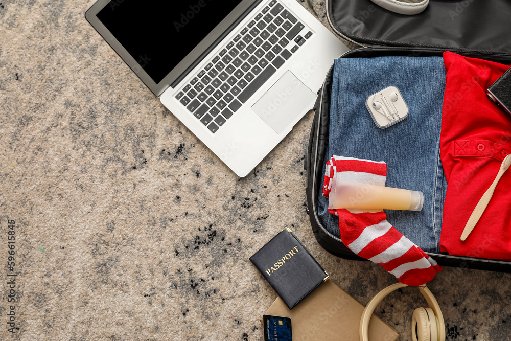 Suitcase with male clothes, laptop and travelling accessories on color carpet