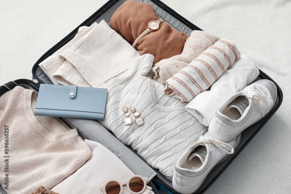 Suitcase with female clothes and accessories on white blanket