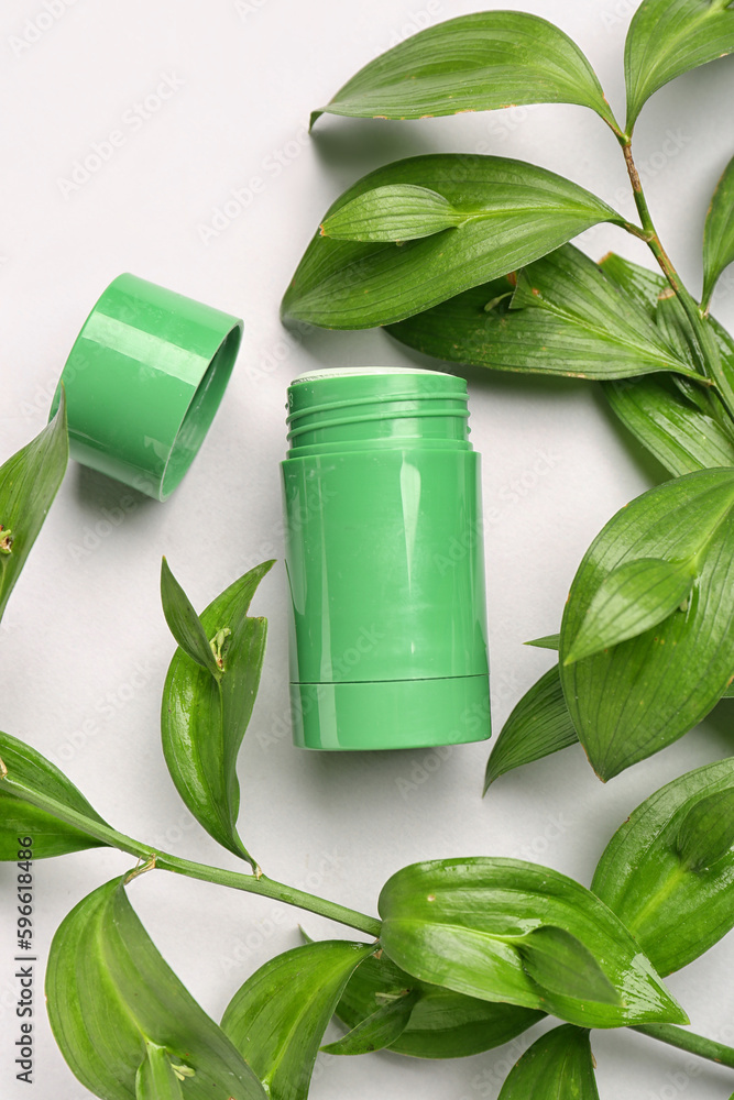 Deodorant bottle and leaves on white background