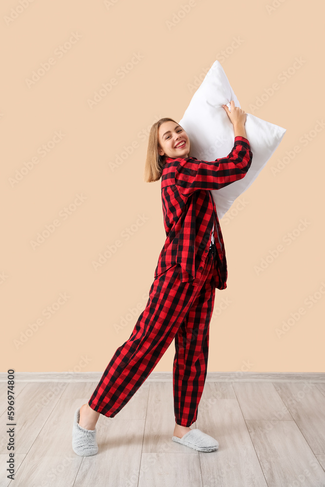 Young woman in pajamas with pillow near beige wall