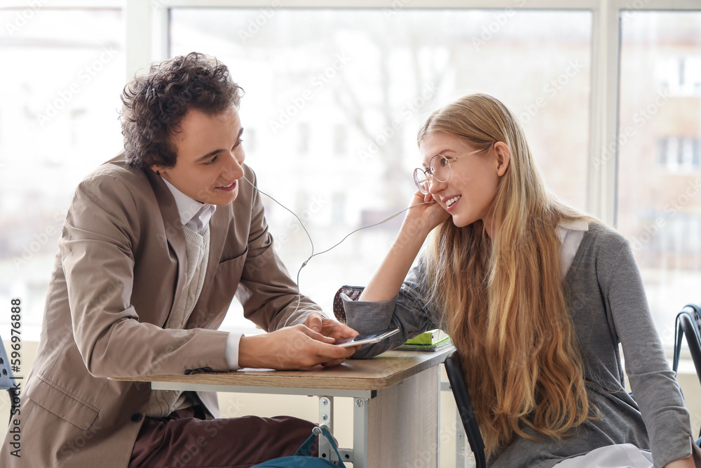 Teenage couple with earphones listening to music in classroom