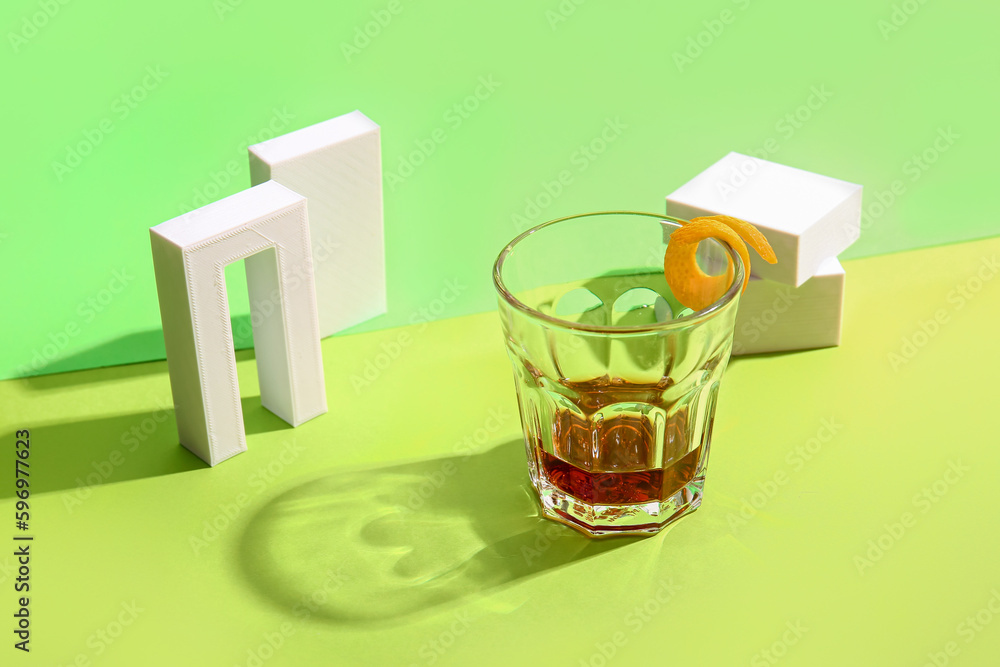 Glass of rum with orange peel and plaster figures on green background