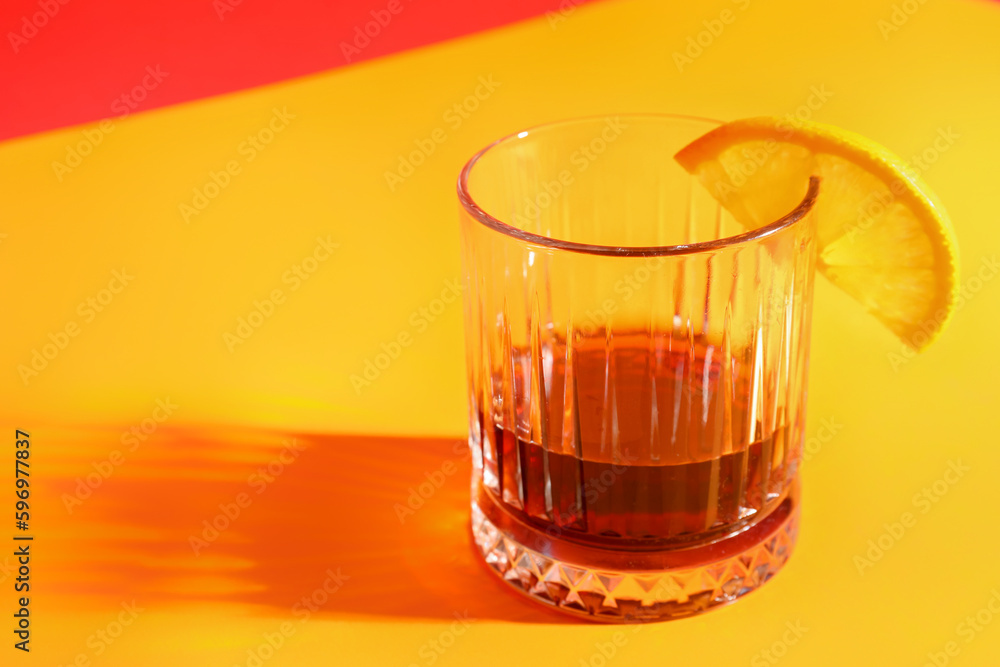 Glass of rum with lemon slice on orange background, closeup