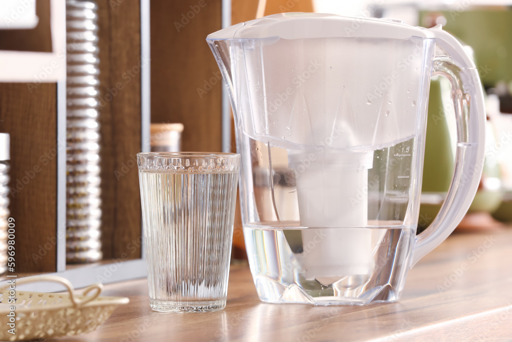 Modern filter jug and glass of water on kitchen counter