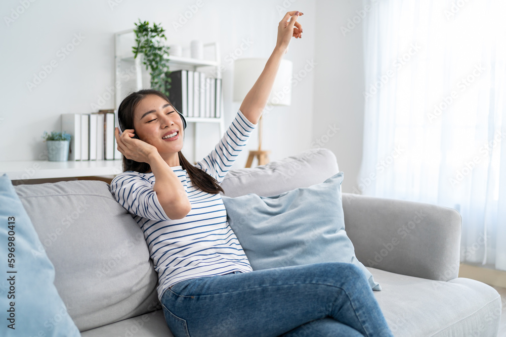 Asian woman listen to music and dancing while sitting on sofa house.