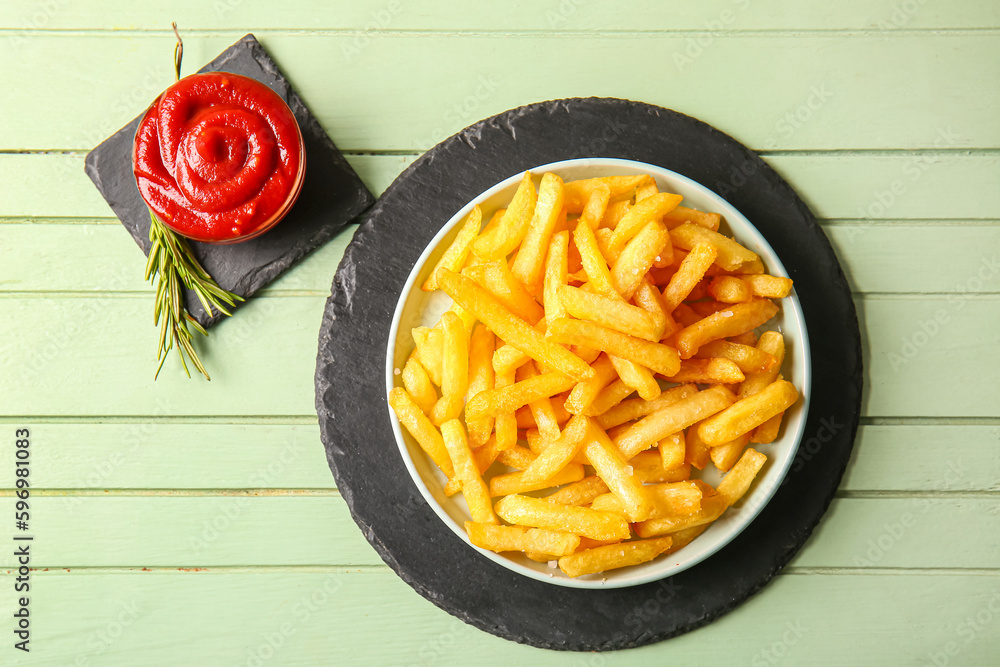 Plate with tasty french fries, bowl of ketchup and rosemary on color wooden background