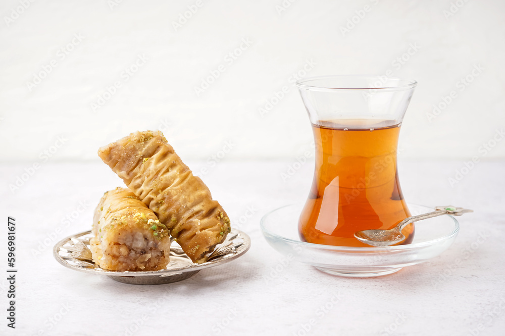 Plate with tasty baklava and glass of Turkish tea on light background