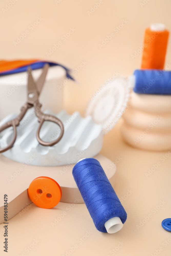 Podiums with thread spools and buttons on beige background, closeup