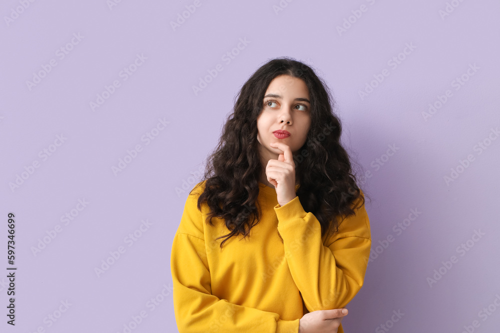 Thoughtful teenage girl in yellow sweatshirt on lilac background