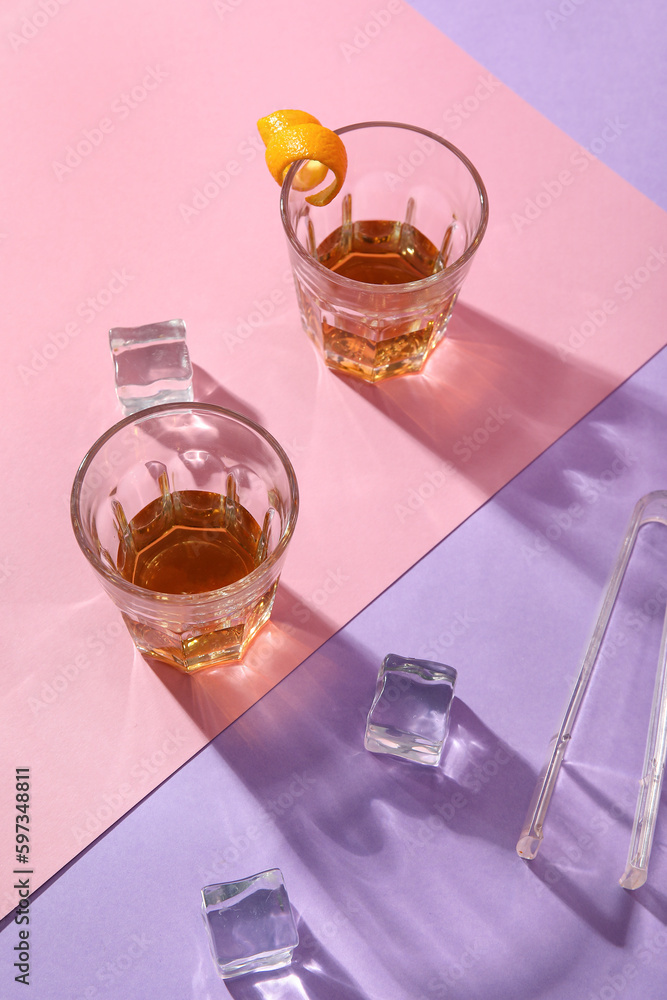 Glasses with rum, ice cubes, tongs and orange peels on colorful background