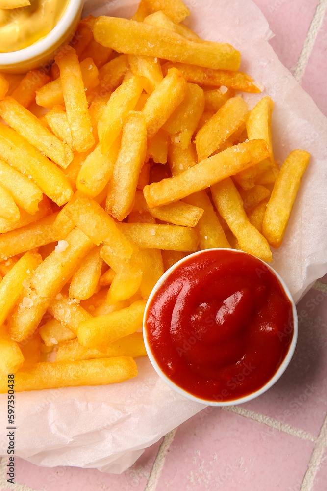 Baking paper with tasty french fries and ketchup on color tile background, closeup