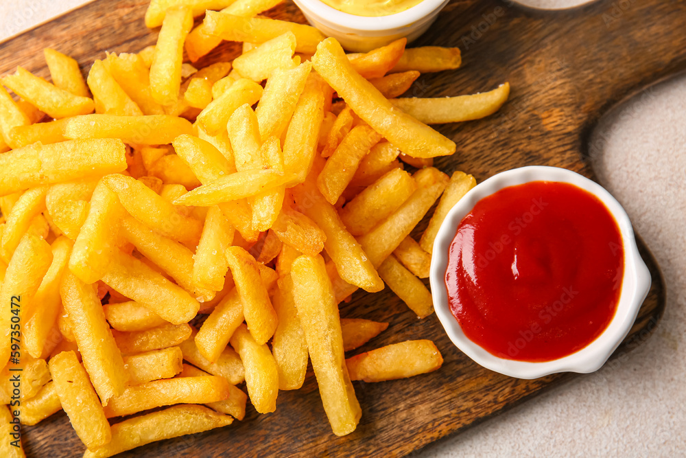 Wooden board with tasty french fries and ketchup on light background, closeup