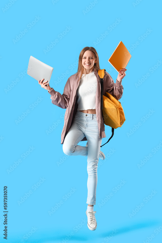 Female student with notebooks jumping on blue background