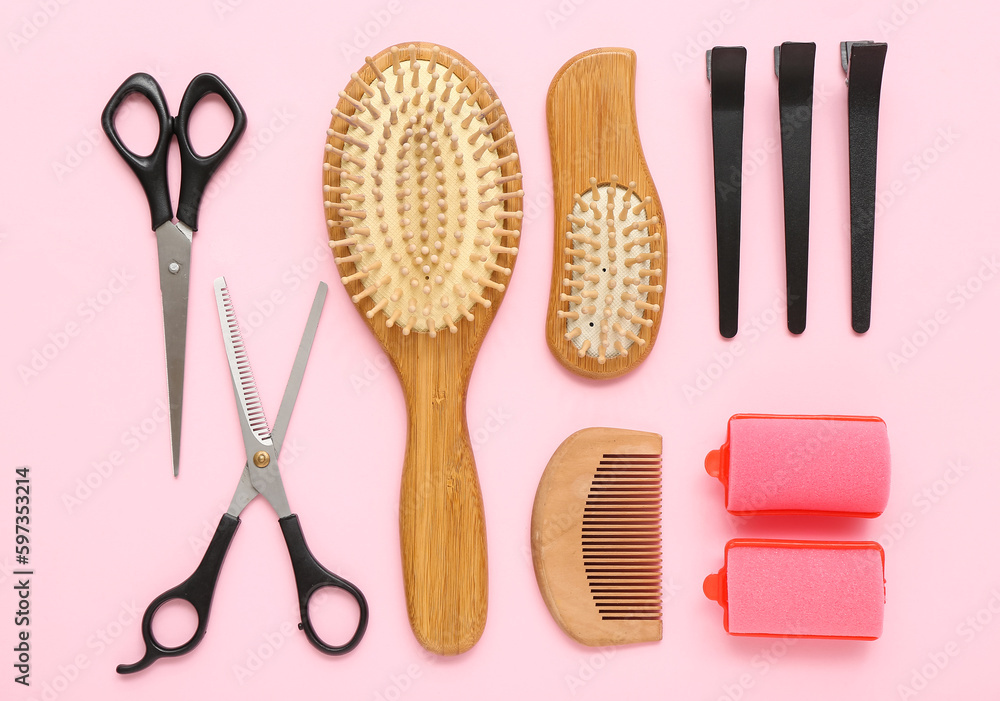 Hair brushes with scissors, clips and curlers on pink background