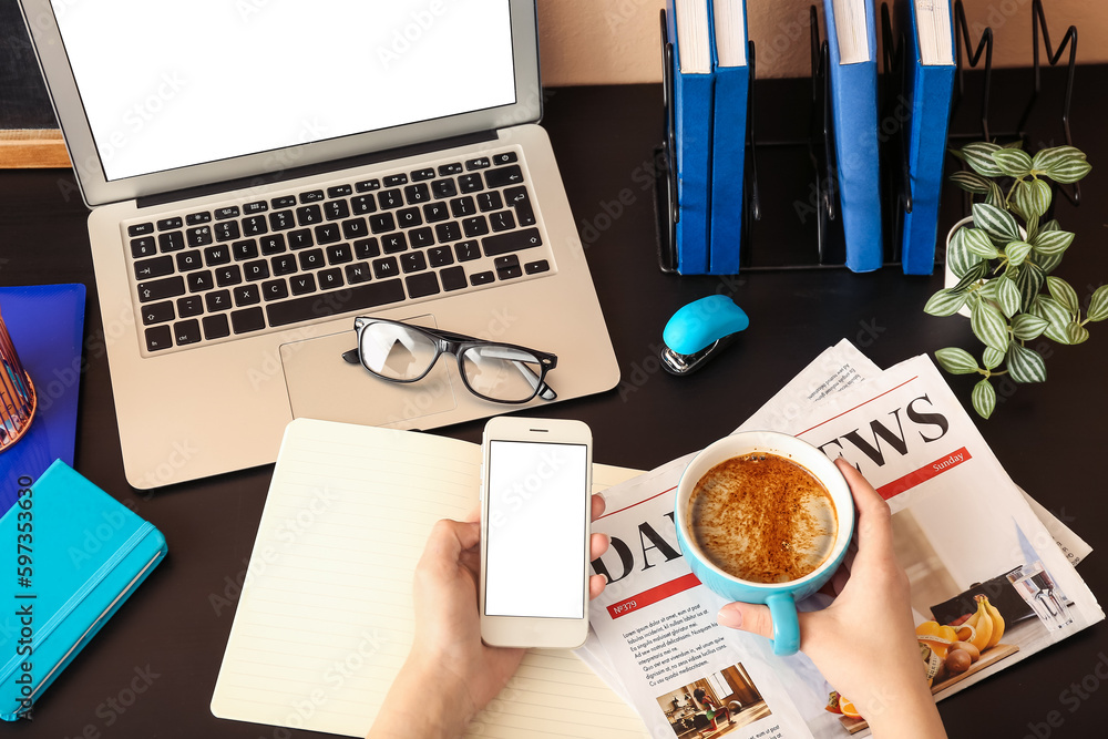 Woman with cup of coffee and mobile phone at table in office, closeup