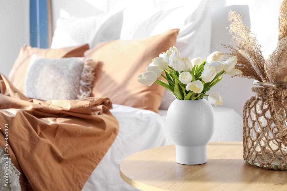 Vases with flowers and pampas grass on table in light bedroom, closeup