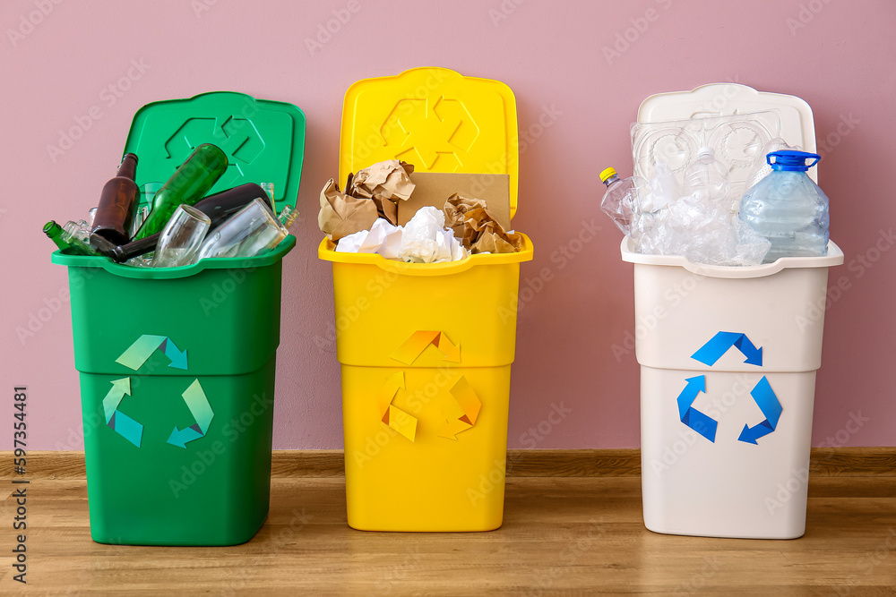 Trash bins with recycling symbol and different garbage near pink wall