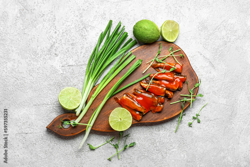 Board with canned fish in tomato sauce, lime, scallions and microgreens on grey table