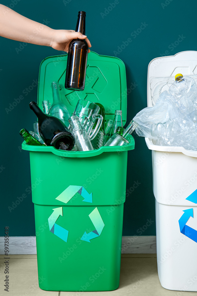 Woman throwing garbage into trash bin near green wall. Recycling concept