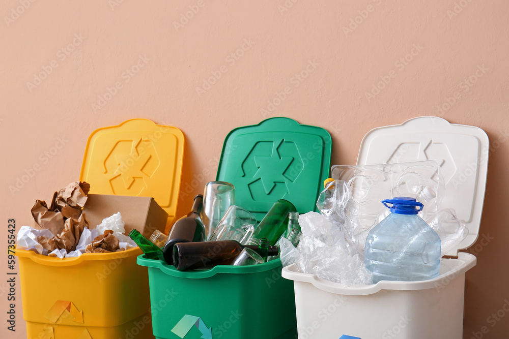 Trash bins with recycling symbol and different garbage near beige wall