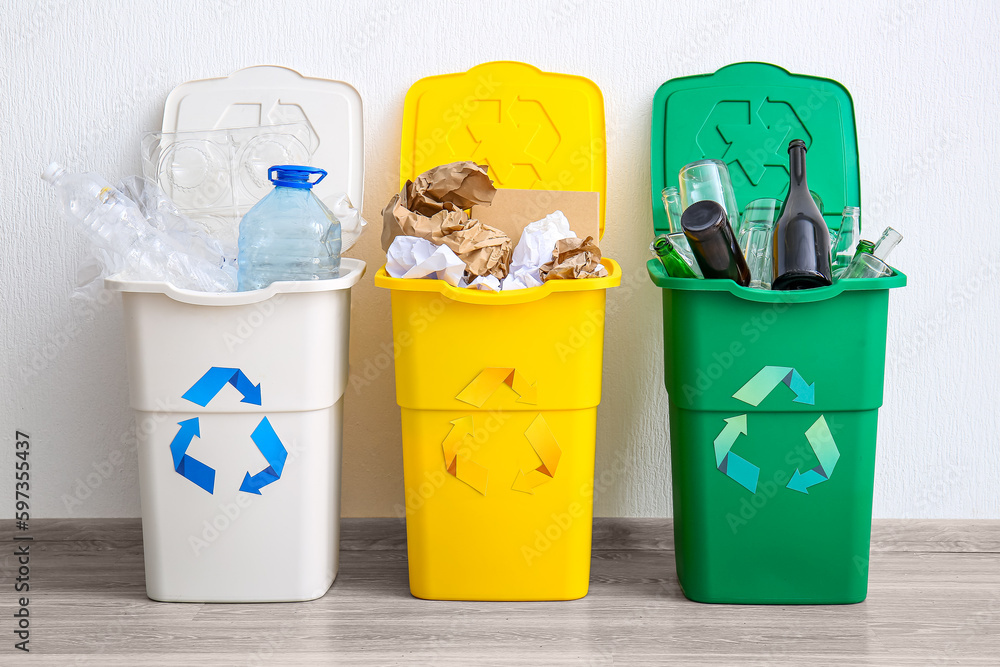 Trash bins with recycling symbol and different garbage near white wall