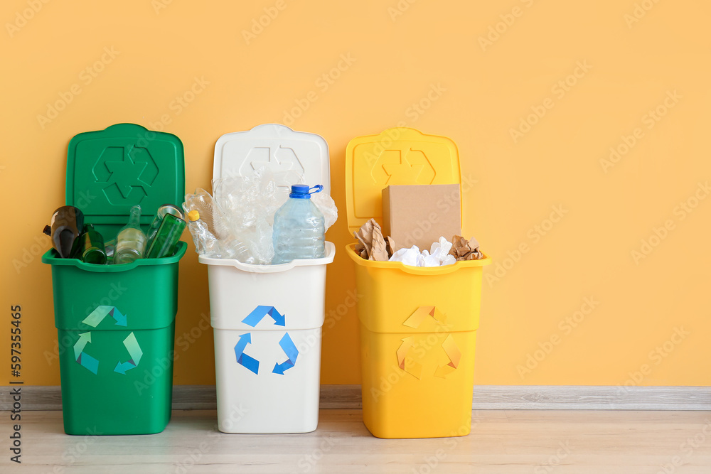 Trash bins with recycling symbol and different garbage near yellow wall