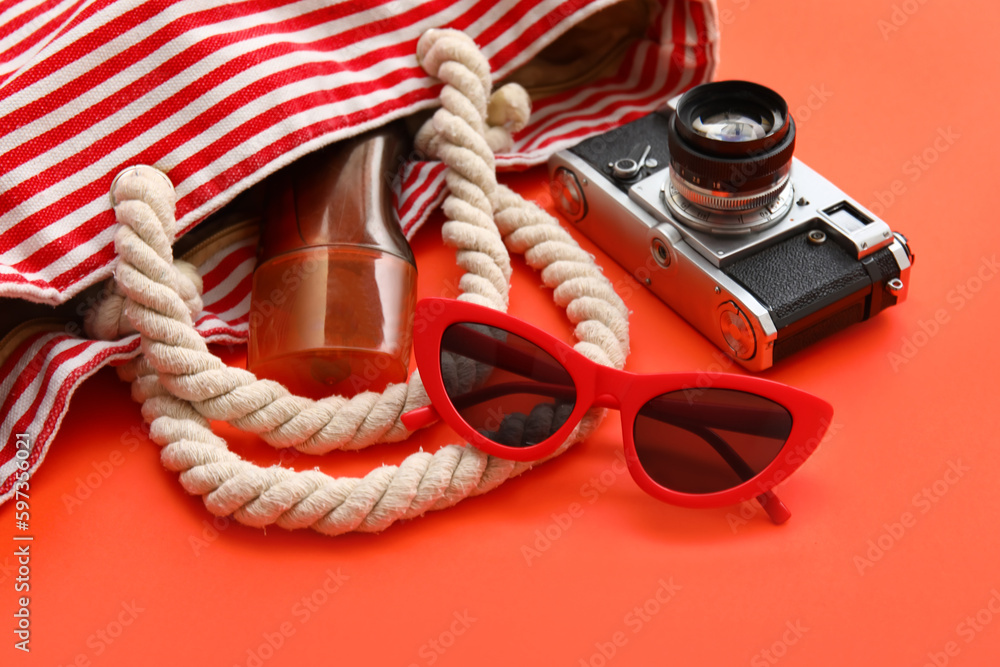 Photo camera, sunglasses, bottle of sunscreen and bag on red background