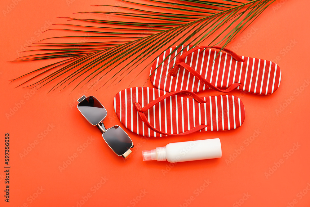 Flip-flops, sunglasses, bottle of sunscreen and palm leaf on red background