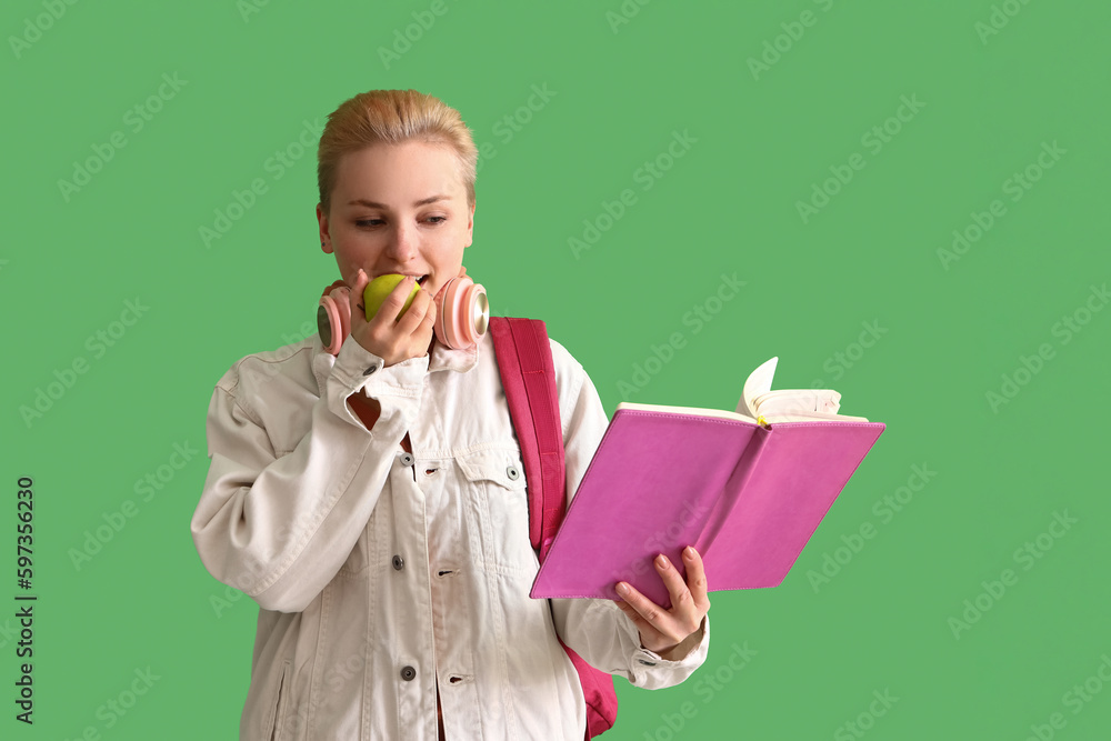 Female student with notebook eating apple on green background