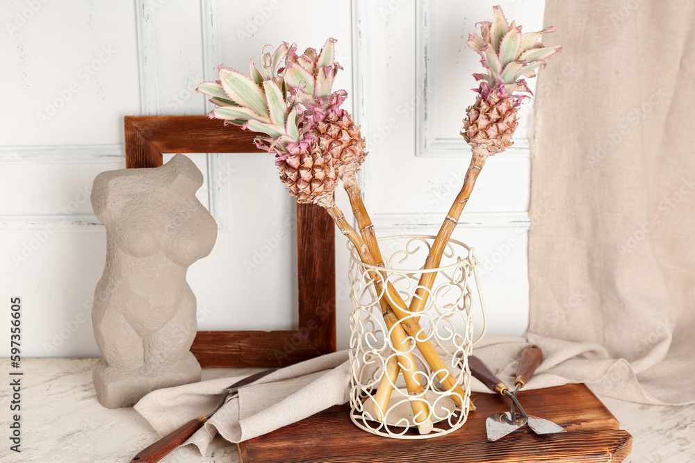 Vase with decorative pineapples, spatulas and decor on table near light wall