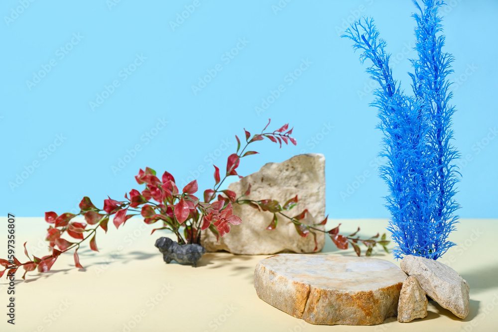 Decorative stone podium and seaweed in sand on blue background