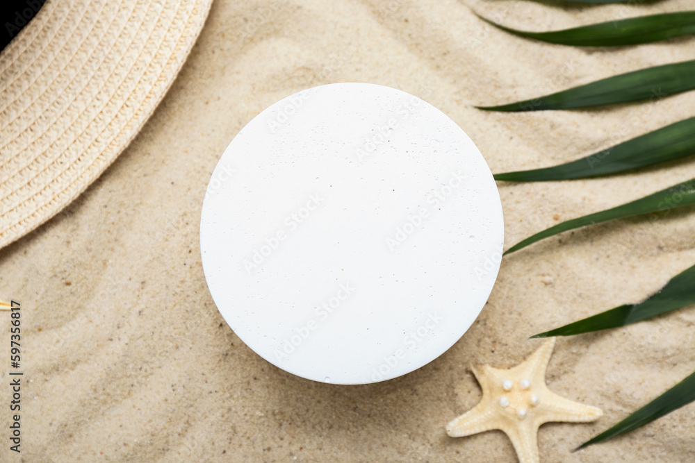 Decorative plaster podium, hat, starfish and palm leaves in sand