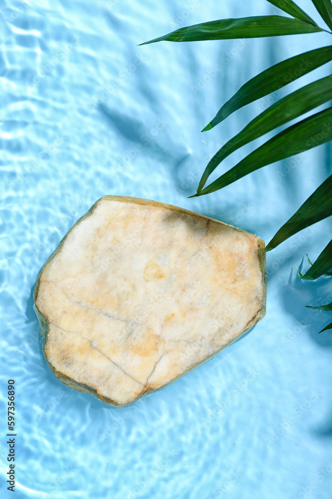 Flat stone and tropical leaves in water on blue background