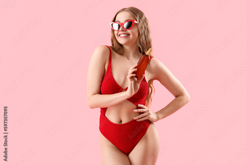 Beautiful young woman with sunscreen cream on pink background